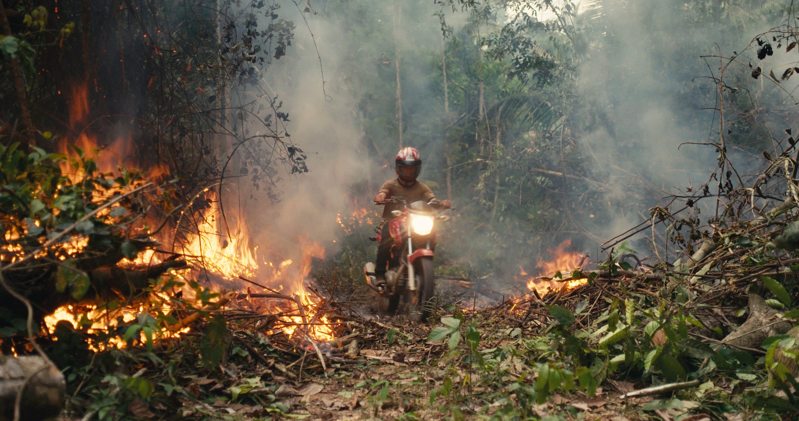 An invader rides his motorcycle through the rainforest fire blaze. (Credit: Alex Pritz/Amazon Land Documentary)