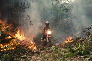 An invader rides his motorcycle through the rainforest fire blaze. (Credit: Alex Pritz/Amazon Land Documentary)